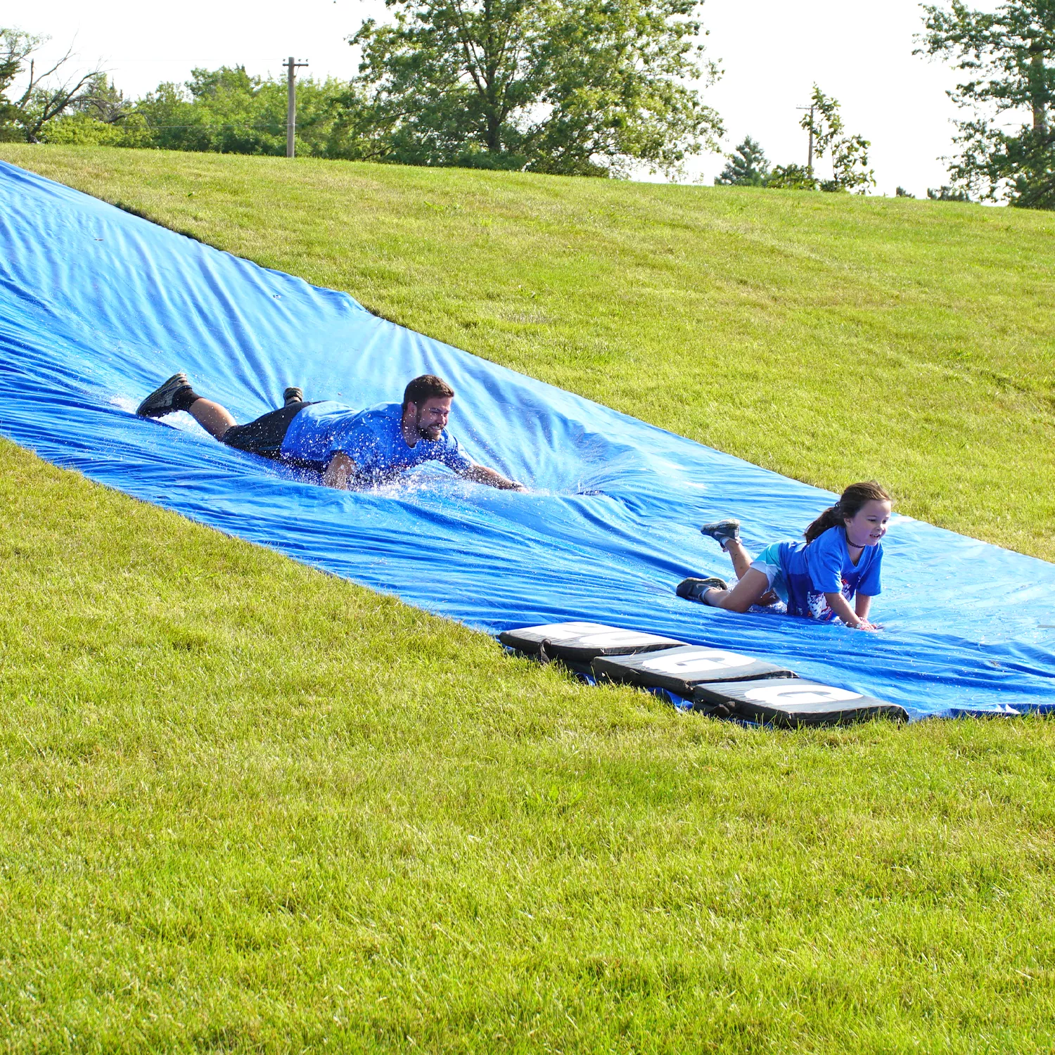 Photo of a father and daughter going down a slip 'n slide at the Youth Sports Adventure Run