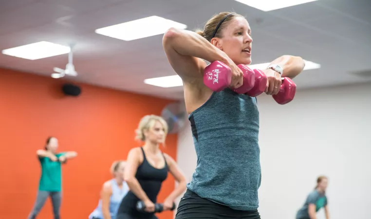 Woman instructor and her class lift free weights during a group exercise class.