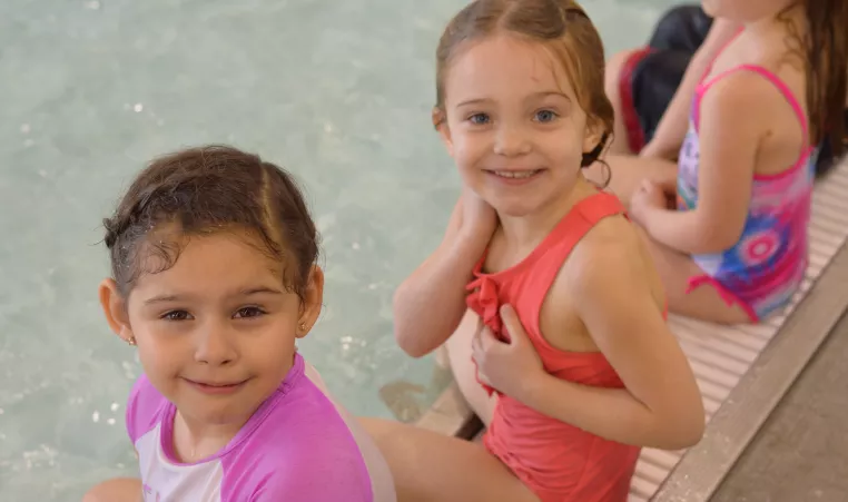 Kids sitting on the edge of an indoor pool at the YMCA