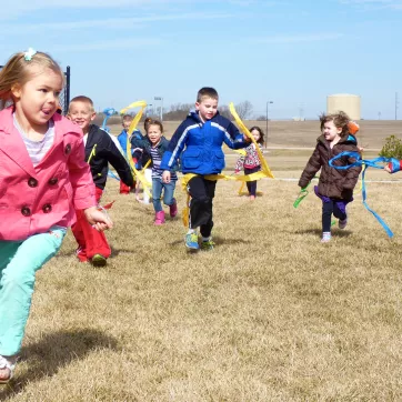 A group of young kids run and wave ribbons outside during their child care program.