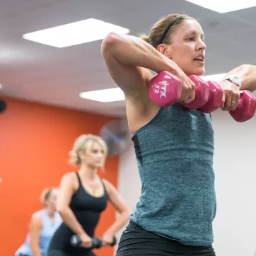 Woman instructor and her class lift free weights during a group exercise class.