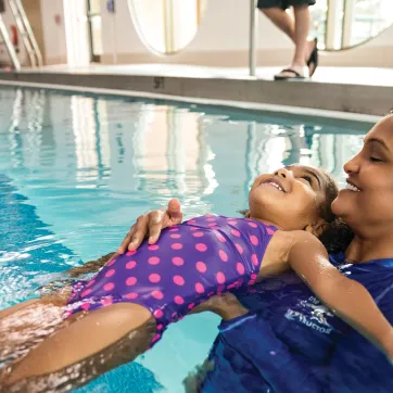 Teacher helps young girl float on her back in the pool.